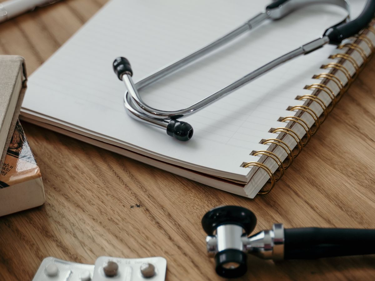 A stethoscope, an otoscope and a notebook on a wooden desk