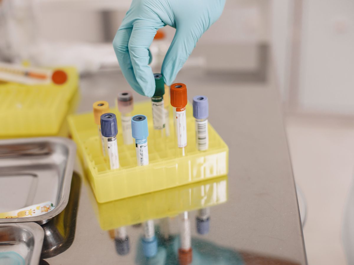 A gloved hand placing a blood collection tube into a laboratory rack