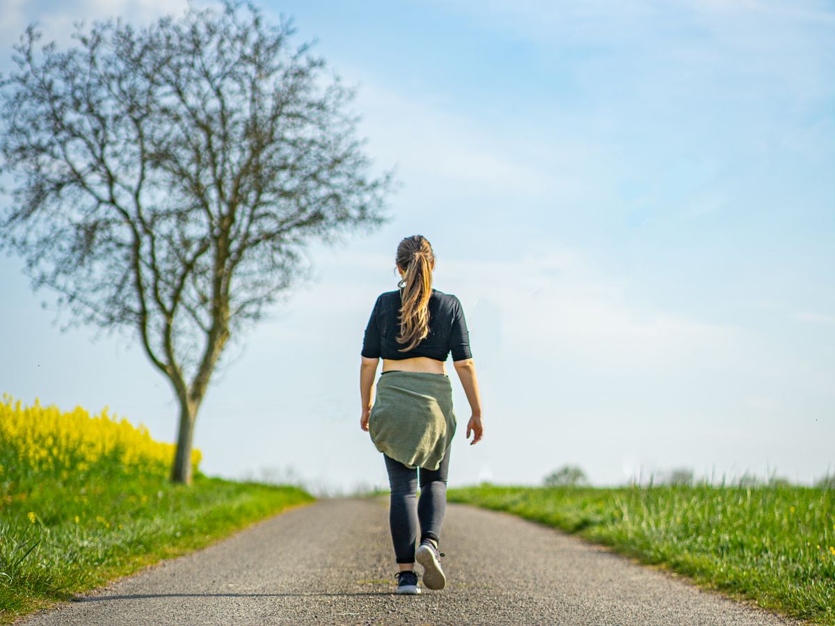 A person walking away along a paved path beside open fields