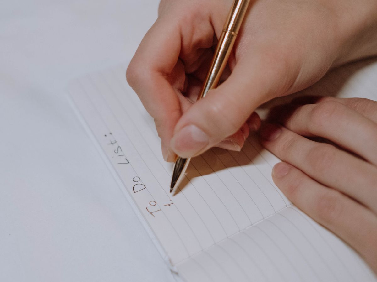 A hand writing a list on a lined notepad